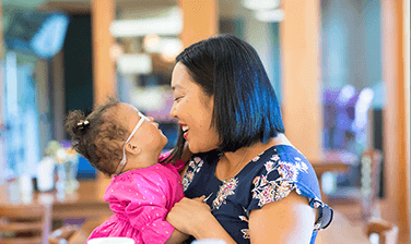 An Ronald McDonald House family, the Burrells, mom Lindsey holding infant Piper, smiling at one another